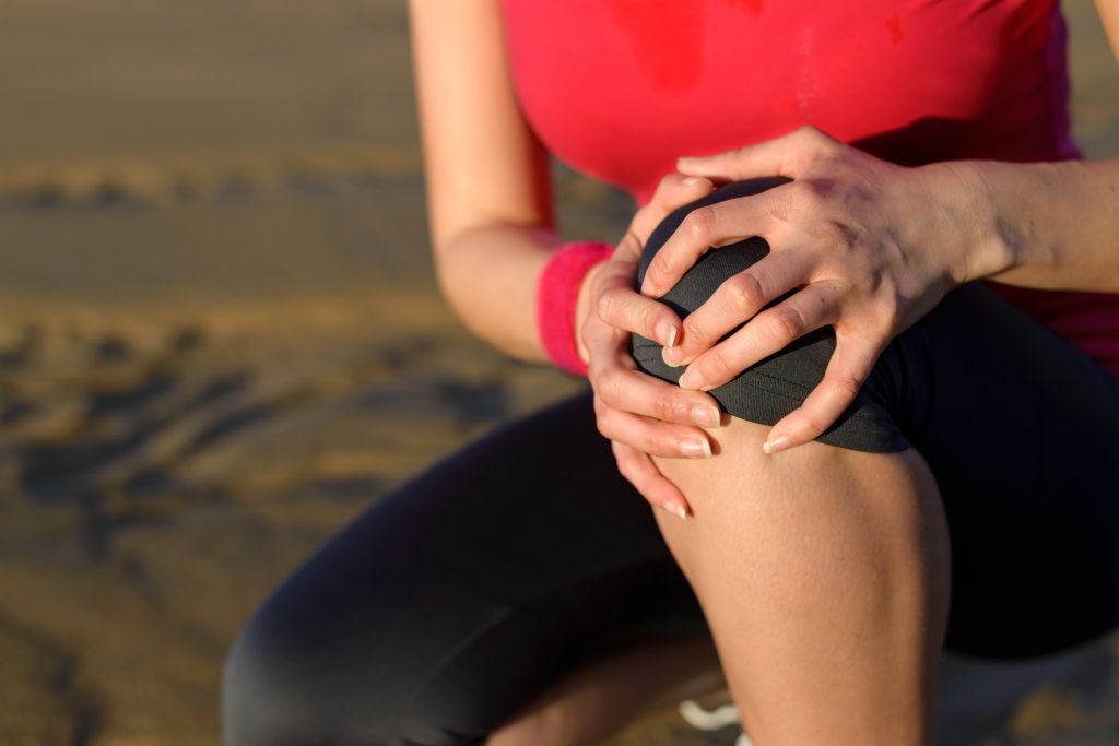 Runner sport knee injury. Woman in pain while running in beach. Caucasian female athlete with painful kneecap.